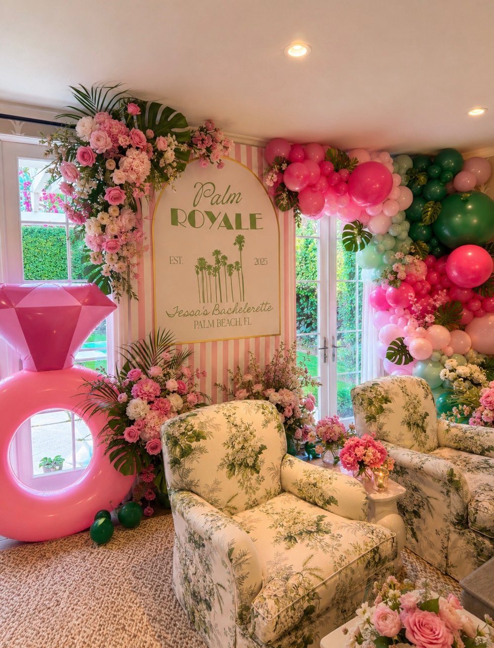 A Palm Royale bachelorette lounge with a pink striped backdrop, floral arches, a giant inflatable diamond ring, balloon wall and floral armchairs