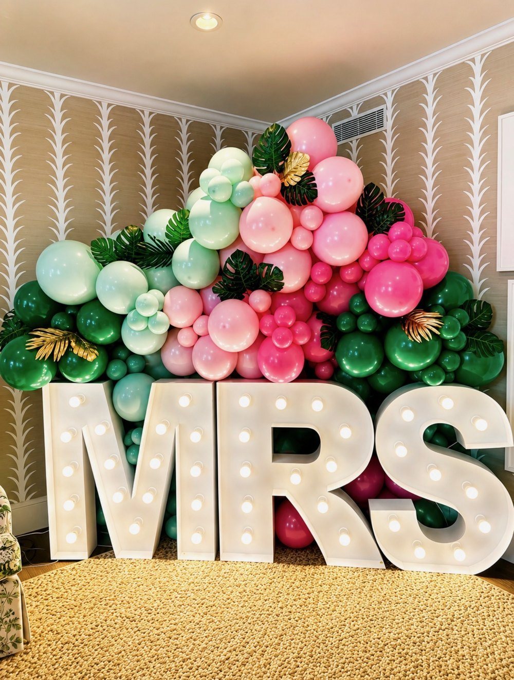 Marquee MRS letters in front of a pink and green balloon garland with tropical leaves