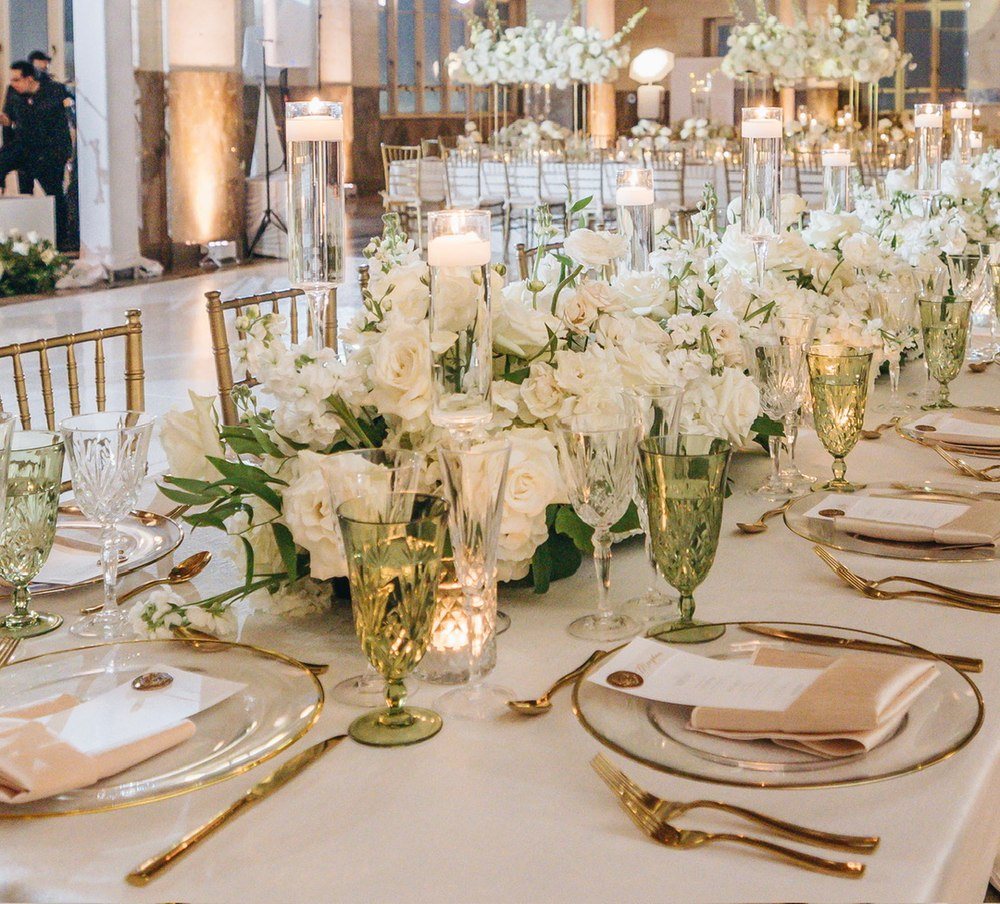 Close-up of a wedding tablescape with white roses, floating candles, green crystal goblets and gold-rimmed chargers