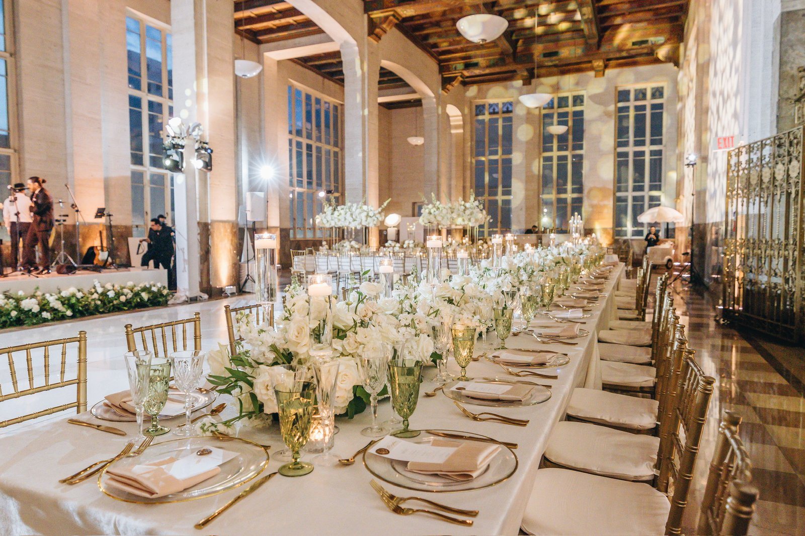 A candlelit wedding reception with long tables of white roses, gold chairs and a live band