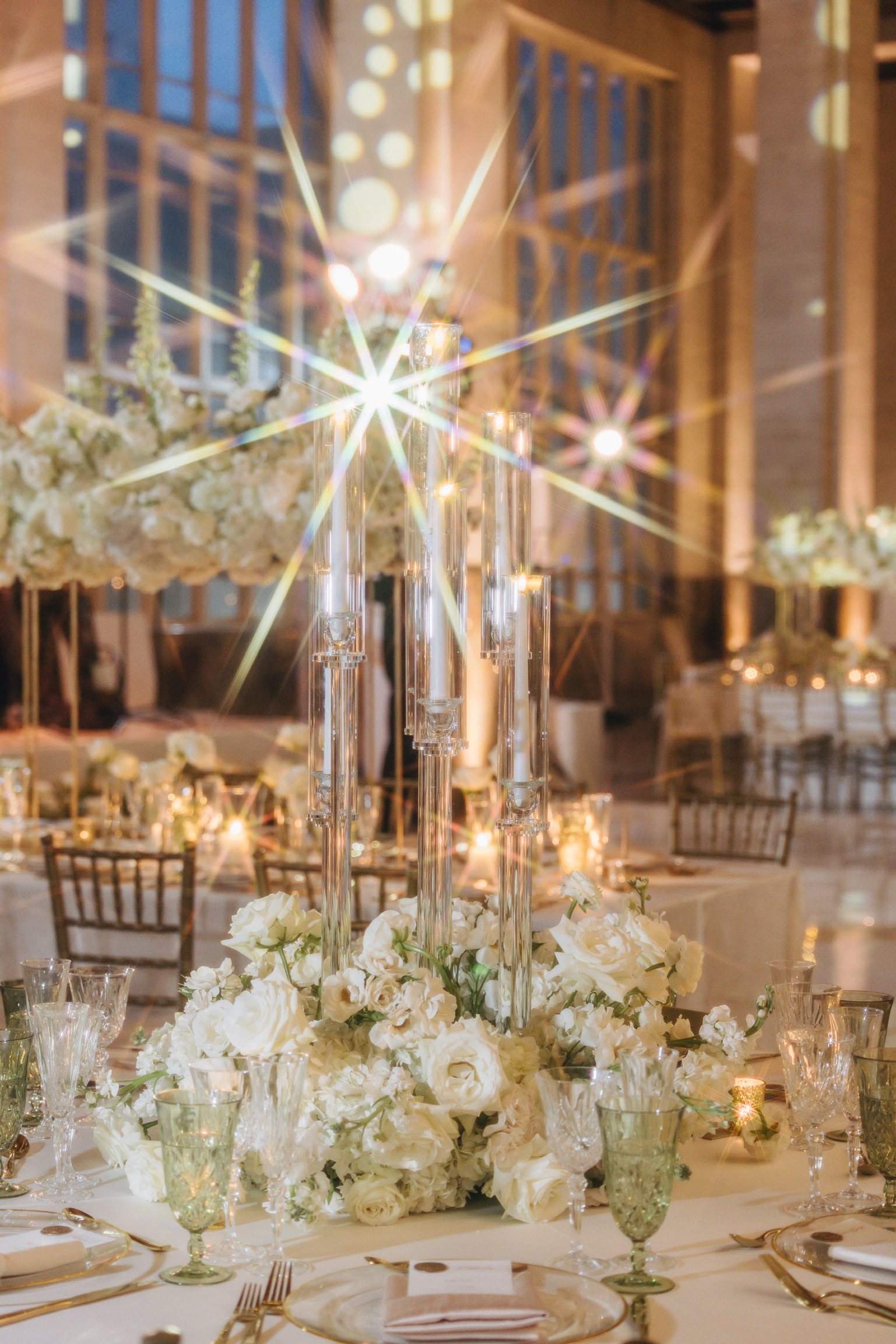 A candlelit reception table with tall crystal candelabras, white rose and hydrangea centerpieces and green crystal goblets
